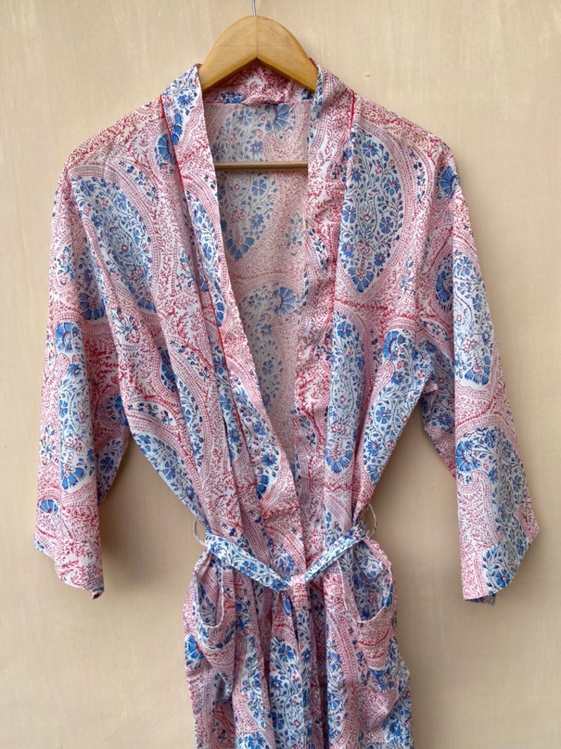 Puede incluir: Una bata de color blanco, azul y rosa con estampado de paisley y cintur&oacute;n de atar. La bata tiene mangas largas y dos bolsillos.