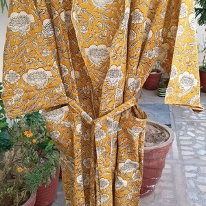 May include: A yellow and white floral print cotton robe with a tie belt. The robe has a long sleeve and a V-neck.