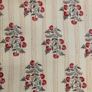 May include: A white cotton fabric with a repeating pattern of red flowers and dark green leaves. The fabric has a subtle texture and is stitched with thin red lines.