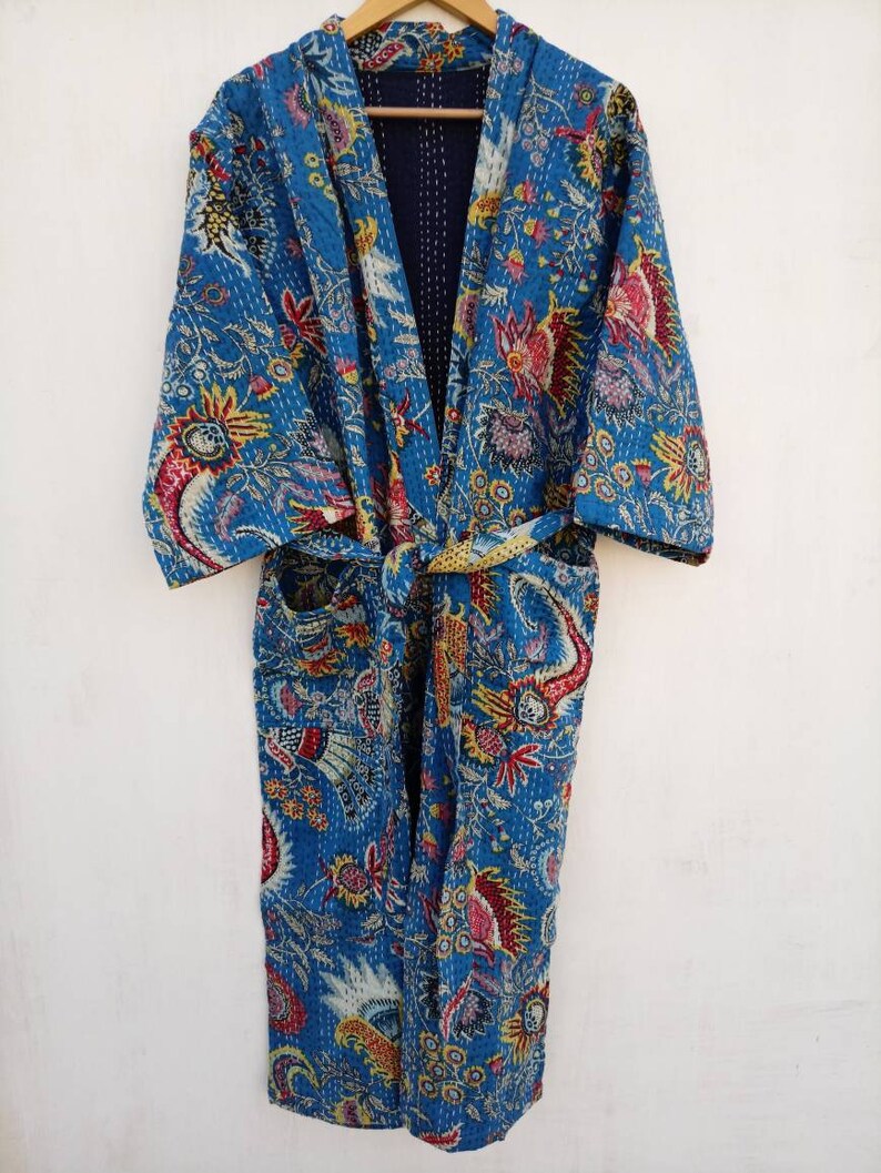 May include: A blue, floral-patterned robe with a tie waist. The robe features a vibrant design with red, yellow, and white accents. The garment is displayed on a wooden hanger against a white background.