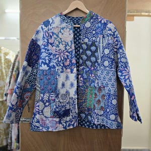 May include: A blue and white quilted jacket with a patchwork design. The jacket has a mandarin collar and a front closure. The fabric is made of cotton and has a soft, comfortable feel.