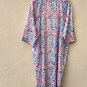 Puede incluir: Una larga bata de color rosa y azul con estampado de paisley y ribete rojo alrededor del cuello y las mangas.