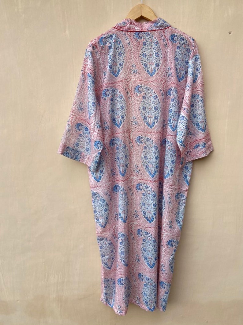 Puede incluir: Una larga bata de color rosa y azul con estampado de paisley y ribete rojo alrededor del cuello y las mangas.