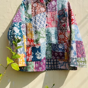 Könnte beinhalten: Eine farbenfrohe Patchwork-Steppjacke mit Stehkragen und Knopfleiste. Die Jacke besteht aus verschiedenen floralen und geometrischen Drucken in Blautönen, Grün, Rosa, Rot und Gelb.