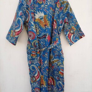 May include: A blue quilted robe with a vibrant floral and paisley pattern. The robe features a matching belt, three-quarter sleeves, and a mandarin collar. The design incorporates red, yellow, and white accents on a blue background.