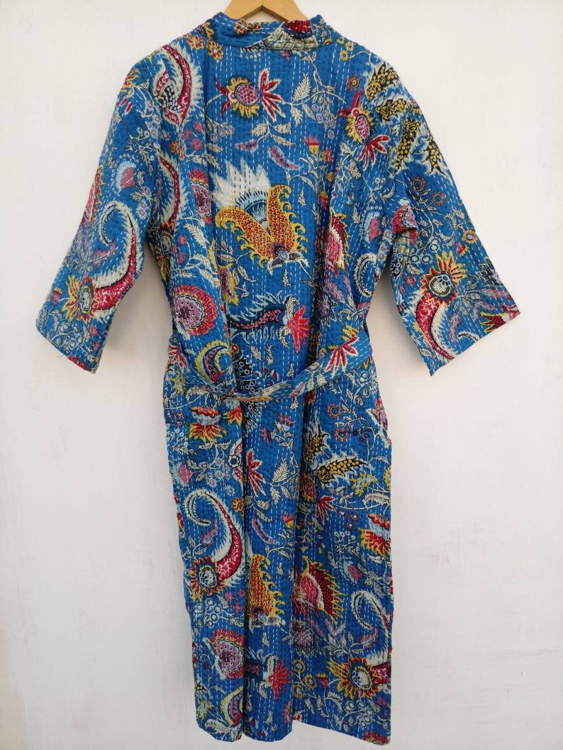 May include: A blue quilted robe with a vibrant floral and paisley pattern. The robe features a matching belt, three-quarter sleeves, and a mandarin collar. The design incorporates red, yellow, and white accents on a blue background.