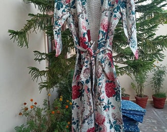 May include: A white floral print robe with a tie belt. The robe features a pattern of large red and pink flowers with green leaves on a white background. The robe is hanging on a wooden hanger.