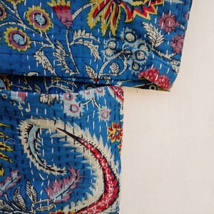 May include: Close-up of a section of a blue quilted fabric with a floral and paisley design. The fabric features a vibrant mix of colors, including red, yellow, and pink, with white stitching. The overall aesthetic is reminiscent of traditional Indian textiles.