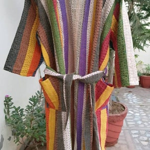 Puede incluir: Una larga bata a rayas con cinturón de anudar. La bata está hecha de un mosaico de diferentes telas en tonos de marrón, amarillo, naranja, verde, morado y blanco. La bata tiene un estilo japonés tradicional.