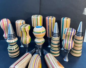 May include: A collection of bottle stoppers featuring handles crafted from multi-colored laminated wood layers. The stoppers display various shapes, including cylindrical, tapered, and bulbous forms, with metallic bases and black rubber rings.