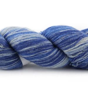Puede incluir: Un ovillo de hilo azul y blanco jaspeado. El hilo está bien enrollado, mostrando una mezcla de azules oscuros y claros con vetas blancas. Ideal para proyectos de punto o ganchillo.