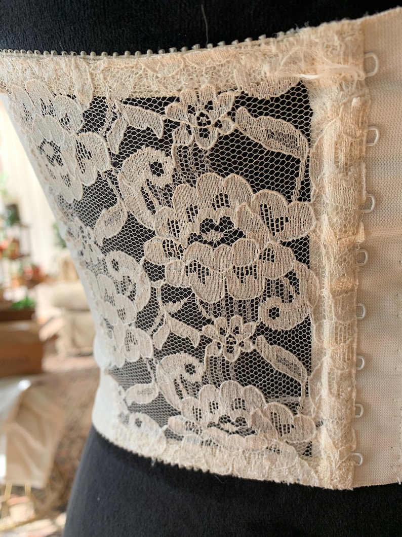 Może przedstawiać: Biały gorset z koronki z zapięciem na haftki i oczka. Koronka jest delikatna i ma kwiatowy wz&oacute;r.