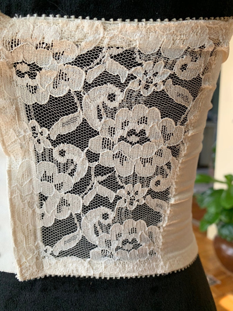 Może przedstawiać: Biała koronka z kwiatowym wzorem. Koronka jest delikatna i ma miękki, kobiecy wygląd.