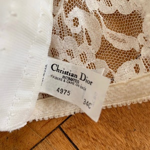 Może przedstawiać: Biała koronka etykieta biustonosza z tekstem "Christian Dior Intimates" i rozmiarem "34C". Etykieta zawiera r&oacute;wnież numer "4975" i tekst "Fibers & Care on Back".