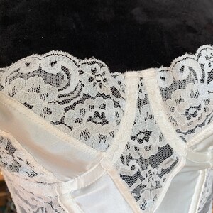 Może przedstawiać: Biały gorset z satyny i koronki z zapięciem na haftki i oczka z przodu. Gorset ma delikatny kwiatowy wz&oacute;r koronki.