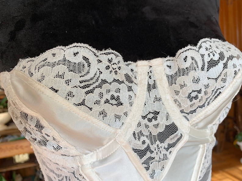 Może przedstawiać: Biały gorset z satyny i koronki z zapięciem na haftki i oczka z przodu. Gorset ma delikatny kwiatowy wz&oacute;r koronki.