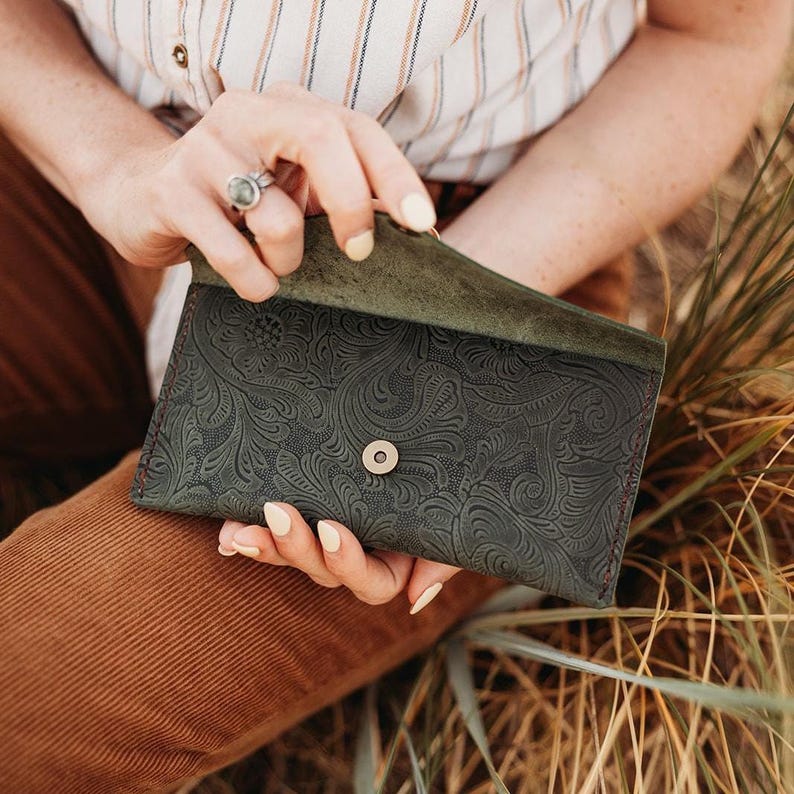 May include: Dark green leather wallet with an embossed floral pattern. The wallet has a snap closure and a contrasting red stitch. The interior is a lighter shade of green. The wallet is open, revealing the inside.