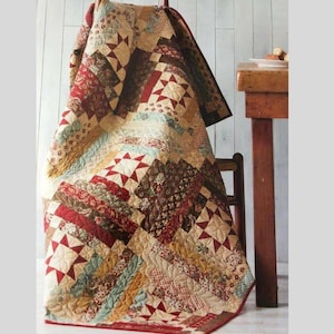 May include: A handmade quilt draped over a wooden chair. The quilt features a patchwork design with various patterns and colors, including red, beige, brown, and green. The quilt's design includes star and stripe patterns.
