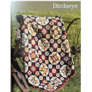 May include: A colorful quilt with a star and square pattern, draped over a rusty metal object. The quilt features a variety of colors including red, yellow, black, and white. The word "Birdseye" is printed at the top of the image.