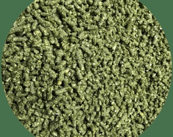 May include: Close-up of a pile of green rabbit food pellets. The pellets are small, cylindrical, and have a slightly rough texture. The color is a mix of green and brown, suggesting a blend of ingredients. The image is set against a green circular background.