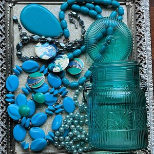 May include: A silver tray with a teal blue glass jar, a teal blue lid, a teal blue oval, and several teal blue necklaces with various beads and charms.