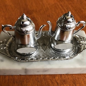 May include: Silver teapot salt and pepper shakers on a marble base with a silver tray.