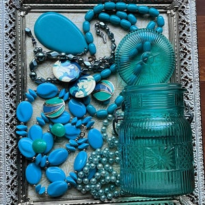 May include: A silver tray with a teal blue glass jar, a teal blue lid, a teal blue oval, and several teal blue necklaces with various beads and charms.