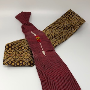 May include: A red and gold patterned tie with a white arrow and red and yellow tassel. The tie is folded and tied with a knot.