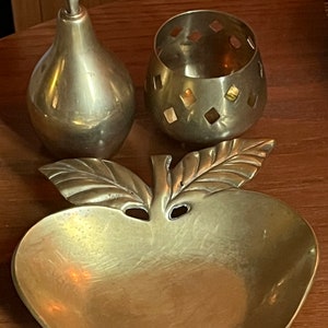 May include: A set of three brass decorative items: a pear-shaped bottle, a small round bowl with a diamond pattern, and a dish shaped like an apple with a leaf.
