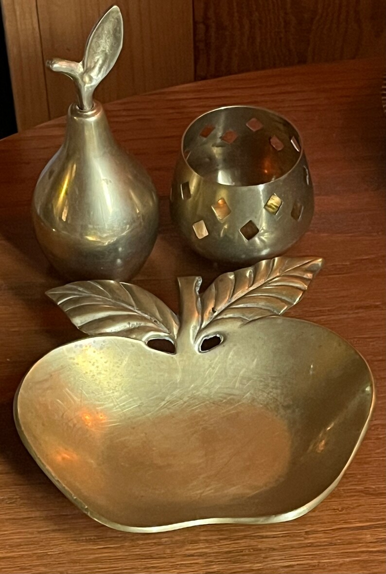 May include: A set of three brass decorative items: a pear-shaped bottle, a small round bowl with a diamond pattern, and a dish shaped like an apple with a leaf.