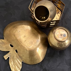 May include: Three brass decorative items, including a bowl with a lattice design, a small bowl with a rounded bottom, and a larger bowl shaped like an apple with a leaf.
