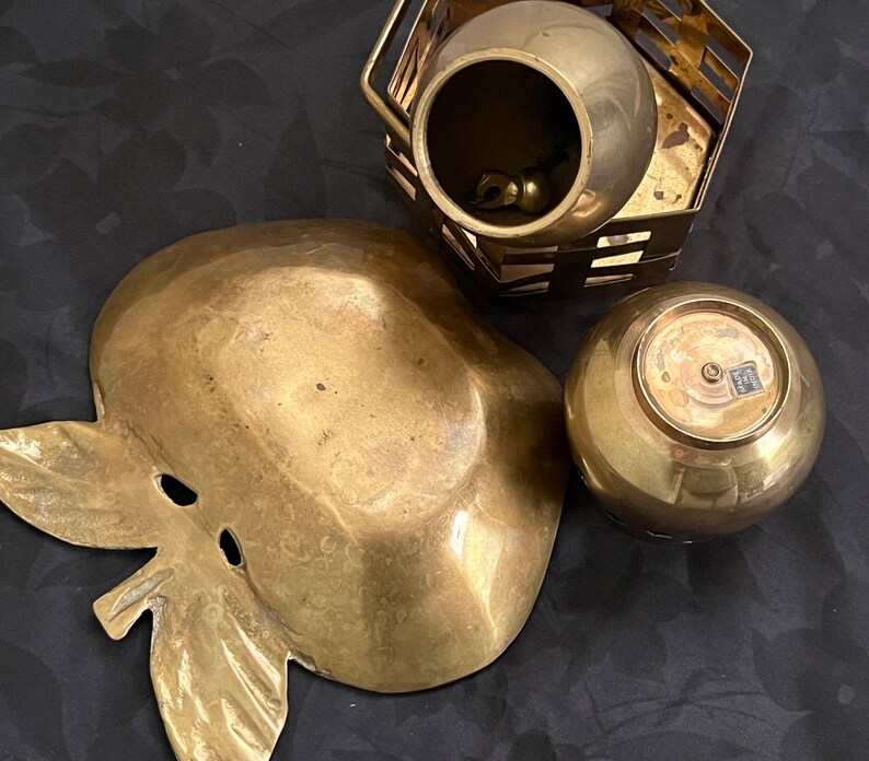 May include: Three brass decorative items, including a bowl with a lattice design, a small bowl with a rounded bottom, and a larger bowl shaped like an apple with a leaf.