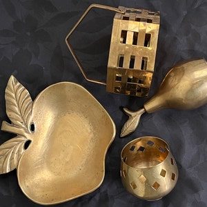 May include: A set of four gold-toned metal decorative items. The items include a small apple-shaped dish, a pear-shaped dish, a small basket with a handle, and a small round dish with a geometric pattern.