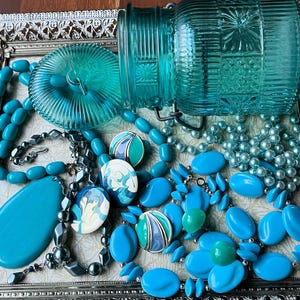 May include: A silver tray with a variety of turquoise blue jewelry and a turquoise blue glass jar with a lid. The jewelry includes necklaces, earrings, and bracelets.