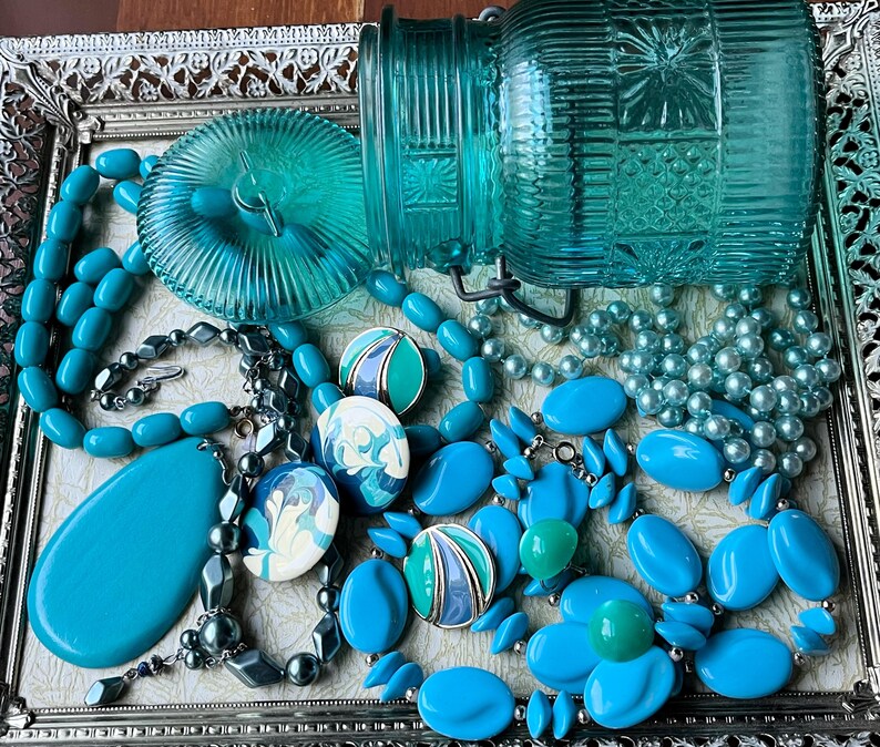May include: A silver tray with a variety of turquoise blue jewelry and a turquoise blue glass jar with a lid. The jewelry includes necklaces, earrings, and bracelets.
