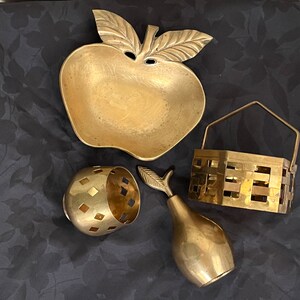 May include: Four brass decorative items: a bowl shaped like an apple, a small bowl with a geometric pattern, a pear-shaped ornament, and a small basket with a woven design.
