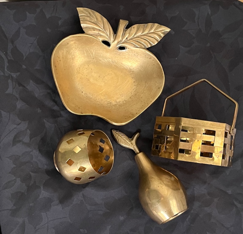 May include: Four brass decorative items: a bowl shaped like an apple, a small bowl with a geometric pattern, a pear-shaped ornament, and a small basket with a woven design.