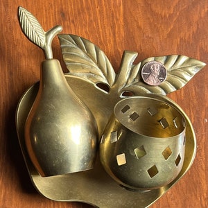 May include: A brass apple shaped dish with a pear and a small bowl with a diamond pattern. The dish has a leaf design on the side.