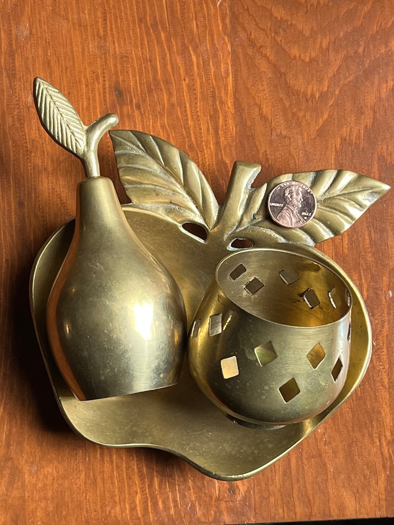 May include: A brass apple shaped dish with a pear and a small bowl with a diamond pattern. The dish has a leaf design on the side.