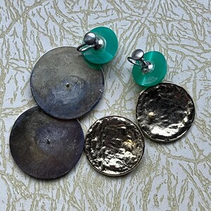 May include: A pair of clip-on earrings with two round discs. One disc is silver and the other is gold. The clip-on part of the earring is green.