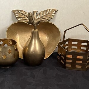May include: Four brass decorative items: a pear-shaped vase, a bowl shaped like an apple with leaves, a small candle holder with a geometric design, and a small hexagonal basket with a handle.