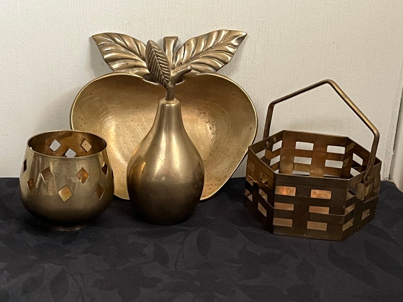 May include: Four brass decorative items: a pear-shaped vase, a bowl shaped like an apple with leaves, a small candle holder with a geometric design, and a small hexagonal basket with a handle.