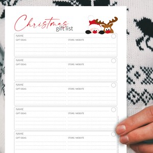 Pu&ograve; includere: Un elenco di regali di Natale bianco con testo rosso e una grafica di Babbo Natale e renne. L'elenco include sezioni per nome, idee regalo e negozio/sito web. L'elenco &egrave; tenuto da una persona che indossa un maglione bianco con un motivo nero.