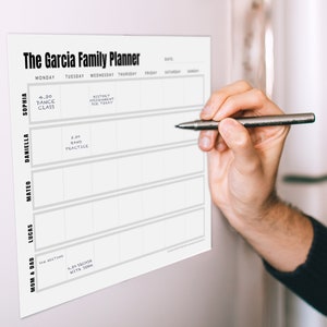 Peut inclure: Un planificateur familial imprimable blanc avec le texte "The Garcia Family Planner" en haut. Le planificateur comporte des colonnes pour chaque jour de la semaine et des lignes pour les diff&eacute;rents membres de la famille. Le planificateur est accroch&eacute; &agrave; un mur blanc.