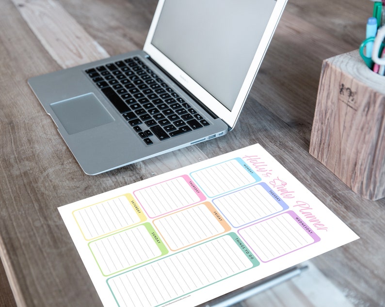 May include: A daily planner sheet with the text "Holly's Daily Planner" in pink script. The planner has boxes for each day of the week, with a "Things to Do" section. A laptop and pen holder are also visible.
