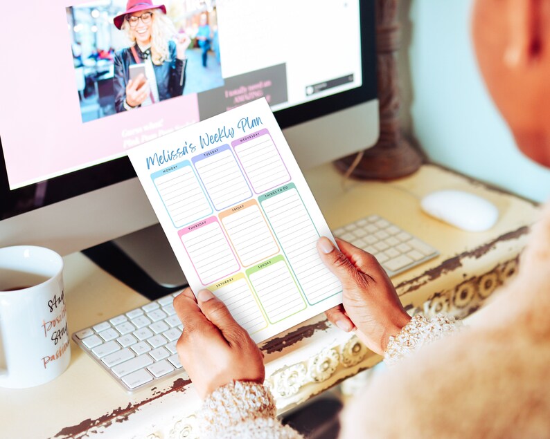 May include: A weekly planner titled "Melissa's Weekly Plan" held in front of a computer screen. The planner has sections for each day of the week, with a space for "Things to Do." The planner's design features pastel colors.