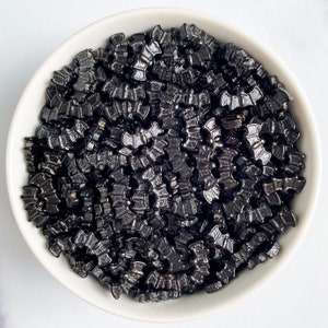May include: A white bowl filled with black bat-shaped sprinkles. The sprinkles are a popular decoration for Halloween baking.
