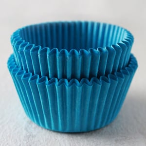 May include: Two blue cupcake liners stacked on top of each other. The liners are made of paper and have a fluted design.