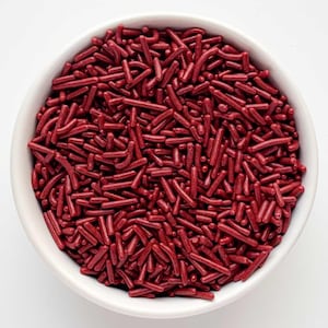 May include: A white bowl filled with red sprinkles. The sprinkles are long and thin, and they are all the same size.
