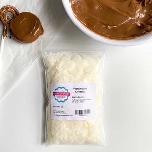 May include: A clear plastic bag filled with white coconut flakes. The bag has a label that reads "Paramount Crystals" and "Confectionery House". The label also lists the ingredients: Hydrogenated Palm Kernel Oil, Soy Lecithin. The bag is labeled with a net weight of 4 ounces.